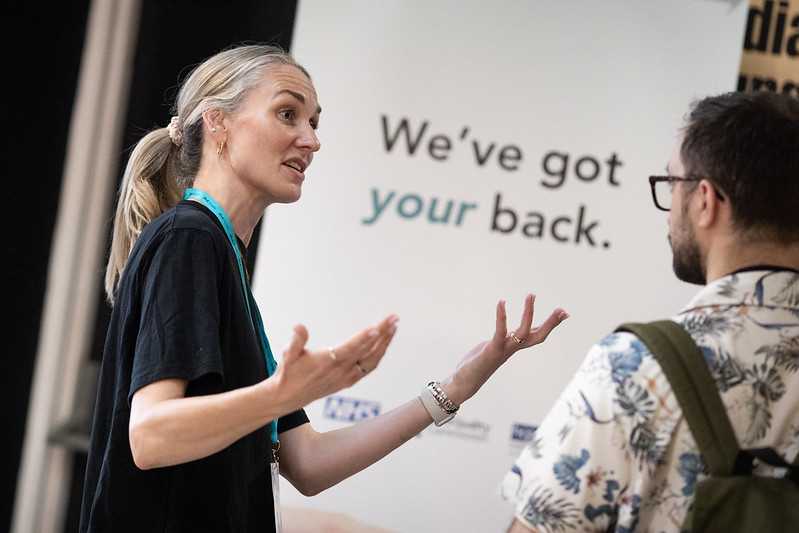 A representative from one of the PyCon UK sponsors talks to an attendee in front of a sponsor banner.