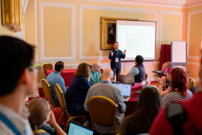 Two people can be seen sitting at desks, intent upon their laptops as they work on the workshop in Cardiff City Hall. A large screen shows information pertaining to the workshop.